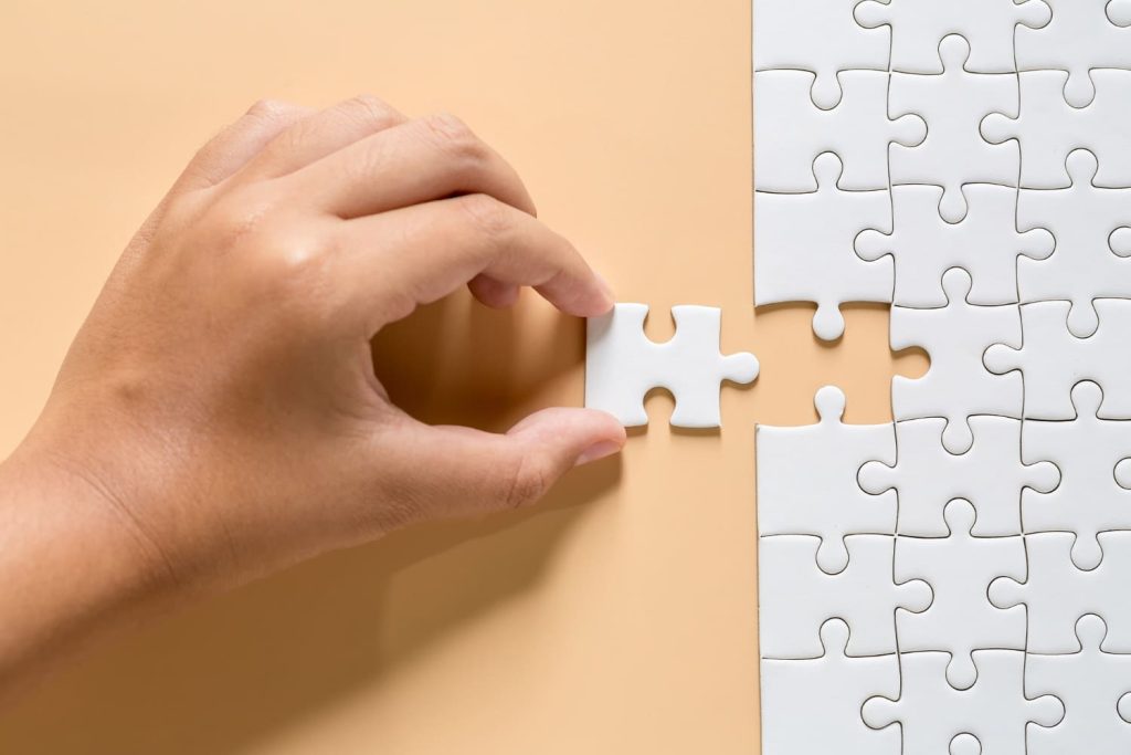 Hand holding the last piece of a white jigsaw puzzle.